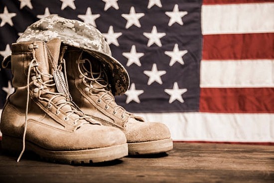 USA military boots, hat and dog tags with American flag in background. No people in this Memorial Day or Veteran's Day image.