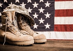 USA military boots, hat and dog tags with American flag in background.  No people in this Memorial Day or Veteran's Day image.
